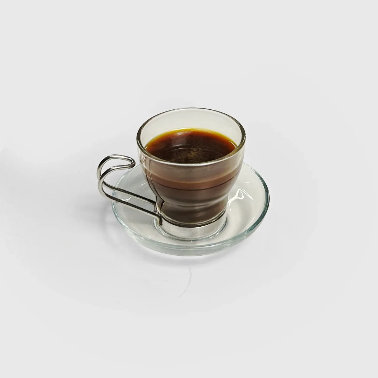 A doppio espresso in a clear demitasse on a saucer